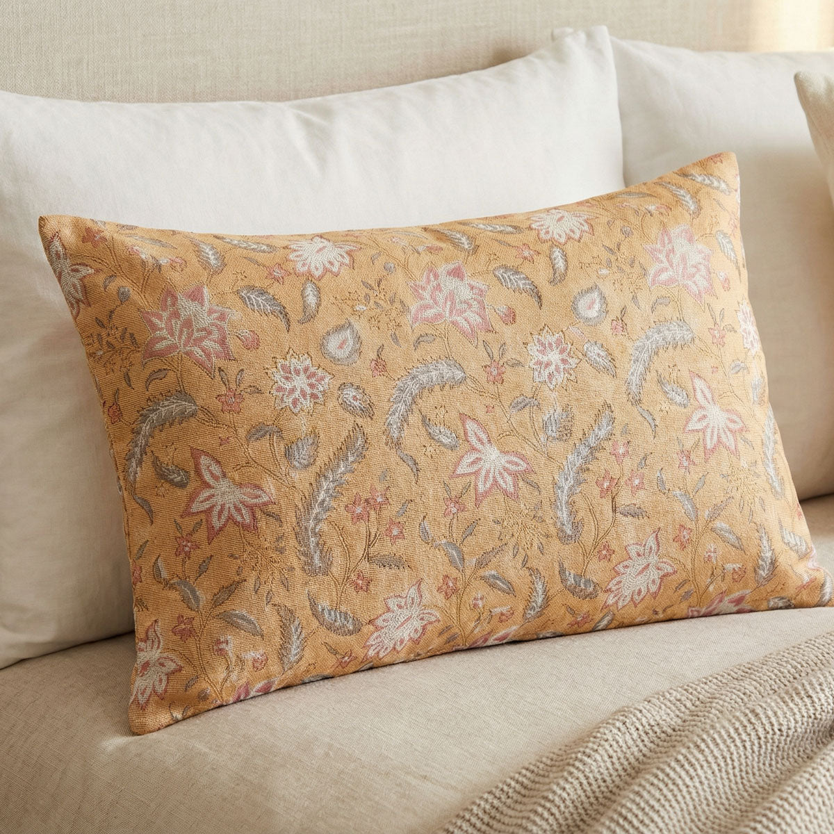 Tan floral cushion styled among cream pillows on a bed