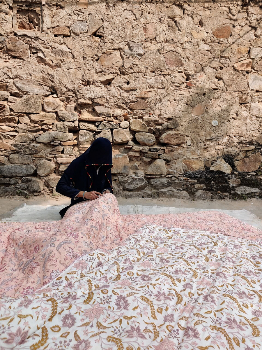 Person holding a large floral-patterned rug against a stone wall.
